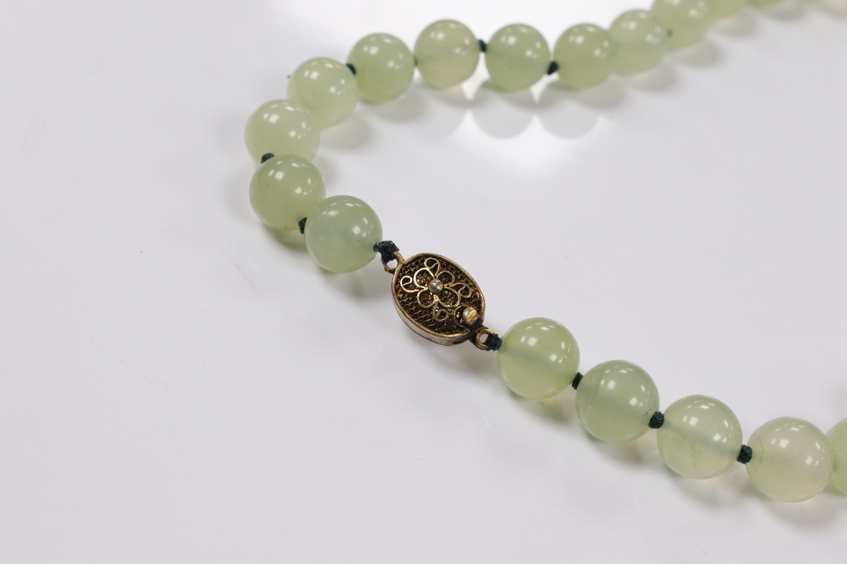 A single strand simulated jade bead necklace, with a gilt metal filigree clasp, 58cm. Condition - fair